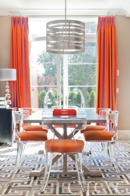modern lucite chairs with orange upholstery make a cool statement in this dining room