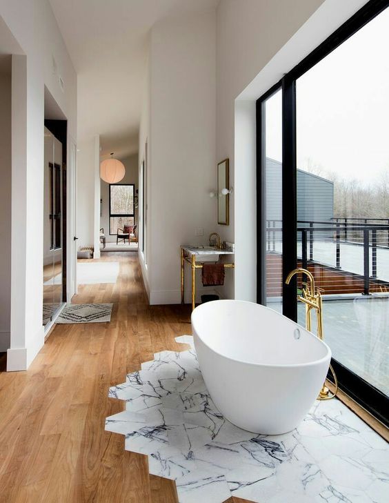 an oval freestanding bathtub next to the glazed wall on marble tiles