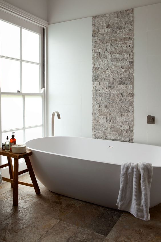 stone tiles and a wooden stool create a textural look and a large bathtub makes you relax