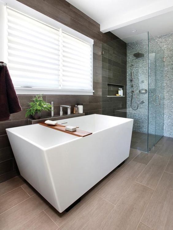 a home spa with a geometric bathtub next to the grey tile wall