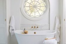 22 a luxury bathroom with a cool rounded window and a freestanding tub with gold accents