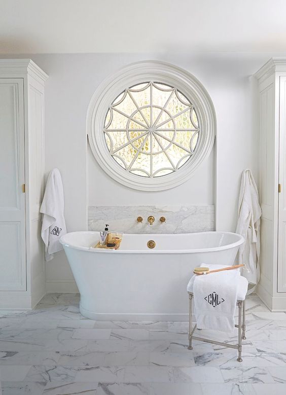 a luxury bathroom with a cool rounded window and a freestanding tub with gold accents