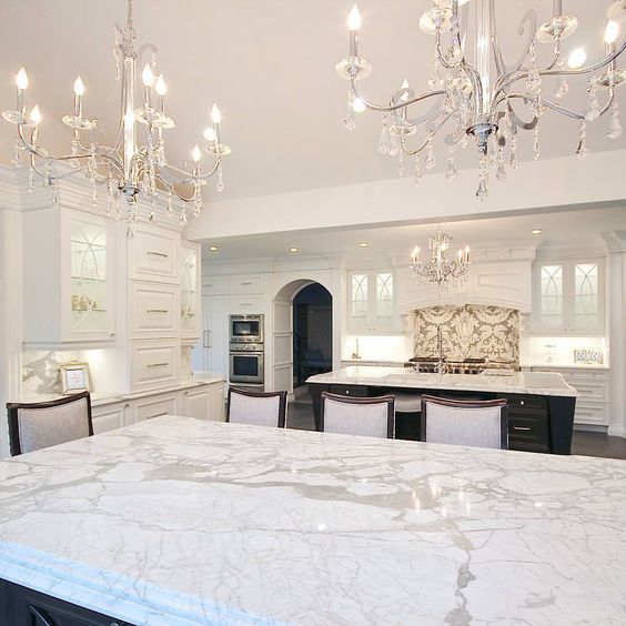 two chic chandleiers with some hanging crystals, marble and lots of white makes the kitchen exquisite