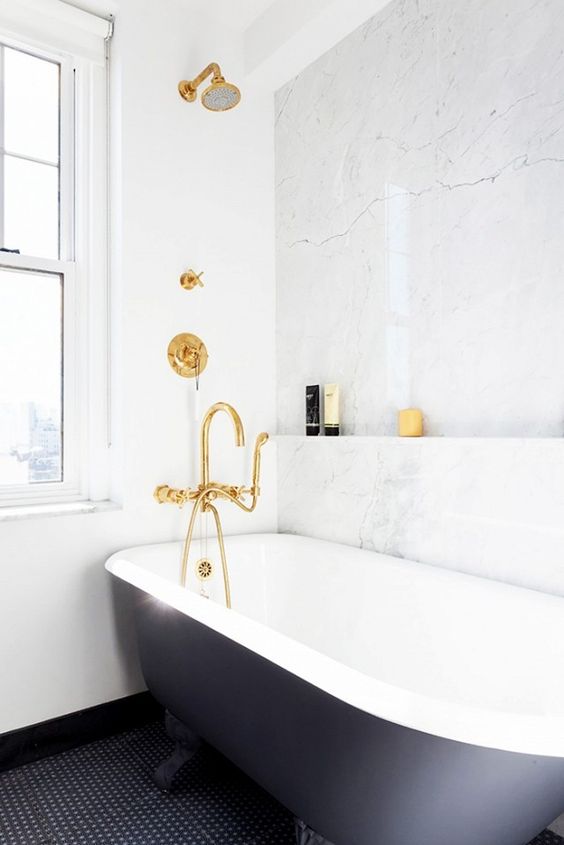brass fixtures, a black tub and a marble wall to shine