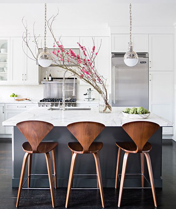 Dark grey kitchen island with a white top and warm colored chairs