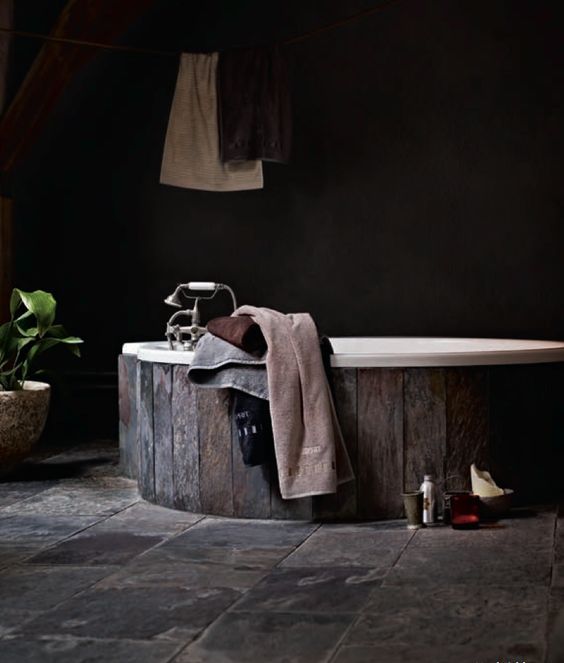 a dark bathroom with a wooden clad bathtub and a stone floor