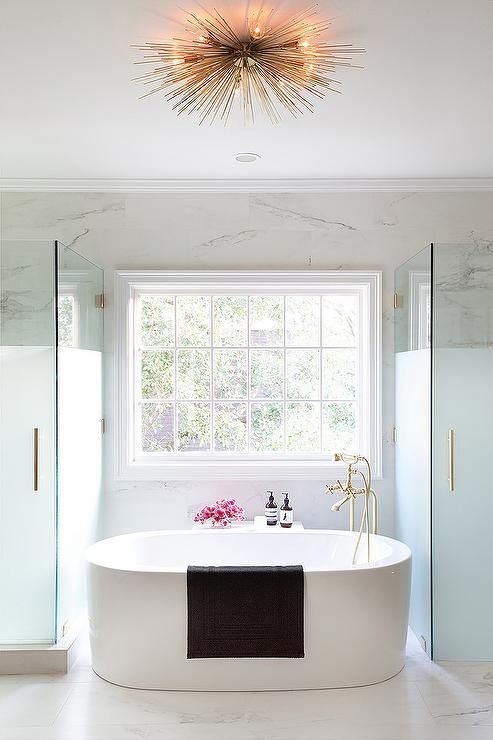 chic master bathroom boasts oval freestanding tub and a brass vintage tub filler placed under a window