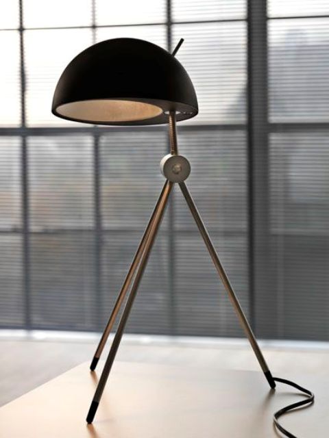 a comfy table lamp on three legs with a black concrete and metal lampshade