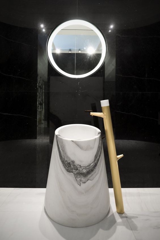 a white marble sink of an eye-catchy shape with a wooden faucet next to it