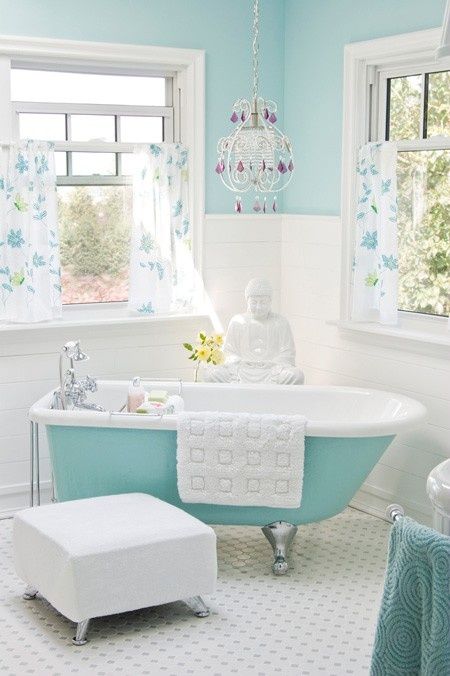 Aqua colored clawfoot tub in a girlish bathroom with a chandelier and floral curtains