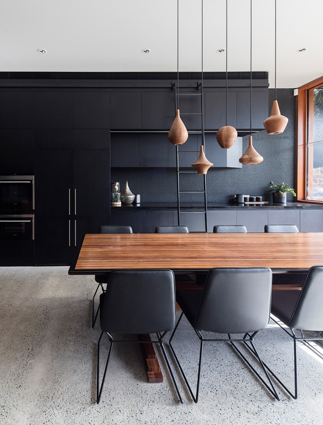 The kitchen features black cabinets, a black penny tile backsplash and a gorgeous wooden dining table with echoing pendants over it