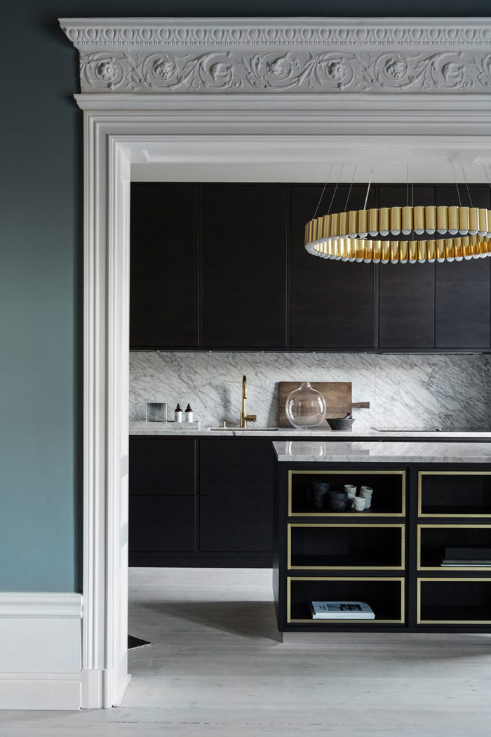 The kitchen is very refined, with dark stained cabinets, brass chandeliers and gilded frame kitchen island
