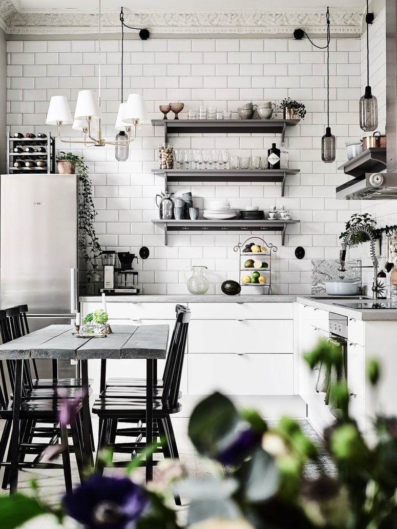 The kitchen is clad with simple white tiles, there are white cabinets and open metal shelves
