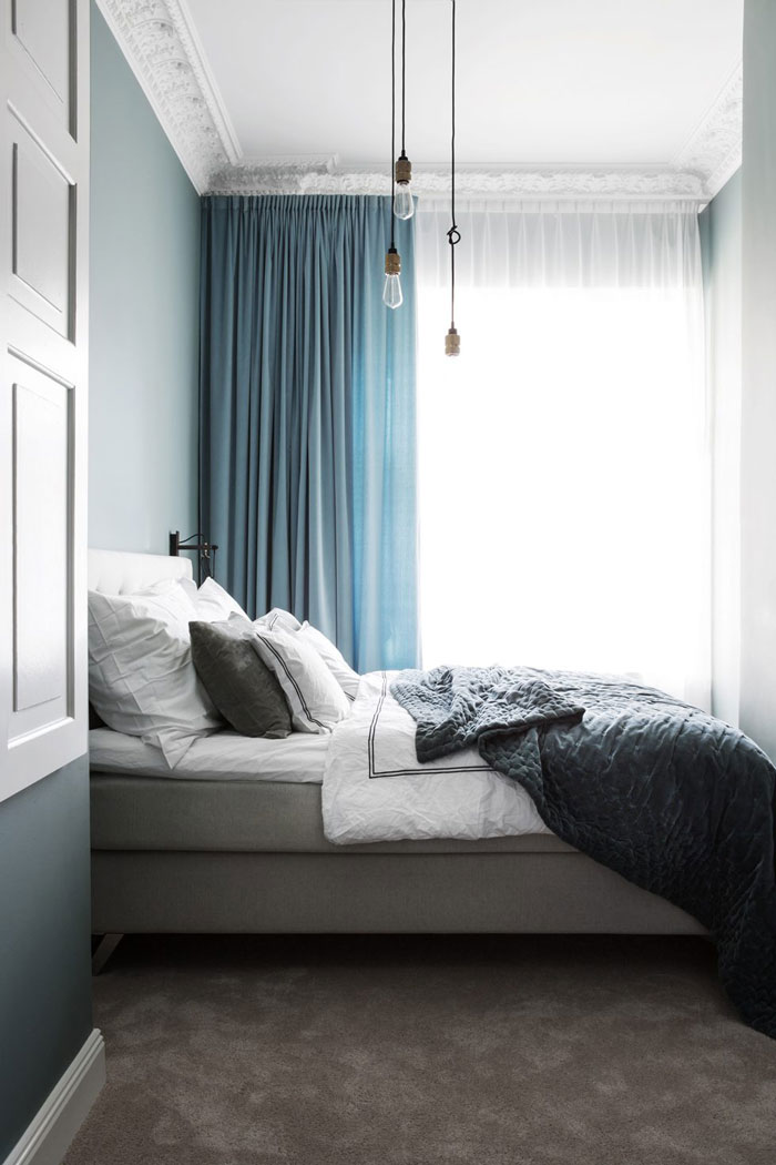 The bedroom is decorated in shades of blue and grey, it's soft and relaxing, and industrial bulbs add a character to the space
