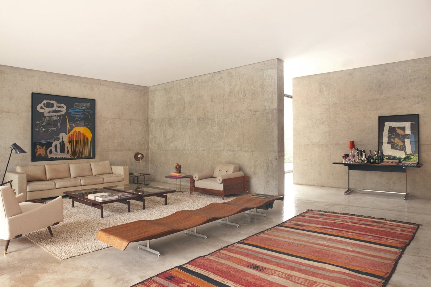 The living room features comfy neutral-colored furniture, a bold artwork piece and some rugs that soften the rough concrete look