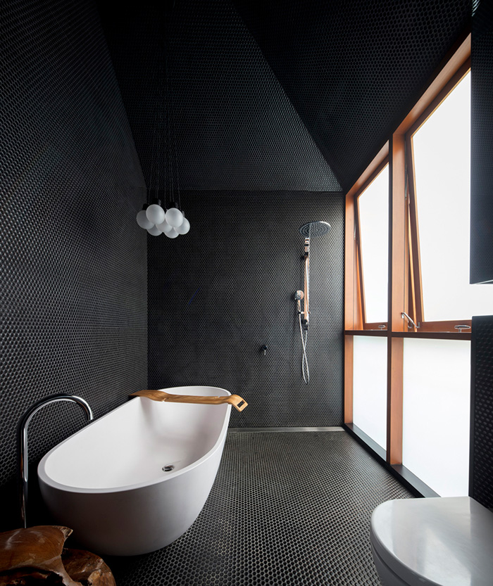 The bathroom is covered with black penny tiles and light-colored wood gives it a more exquisite look