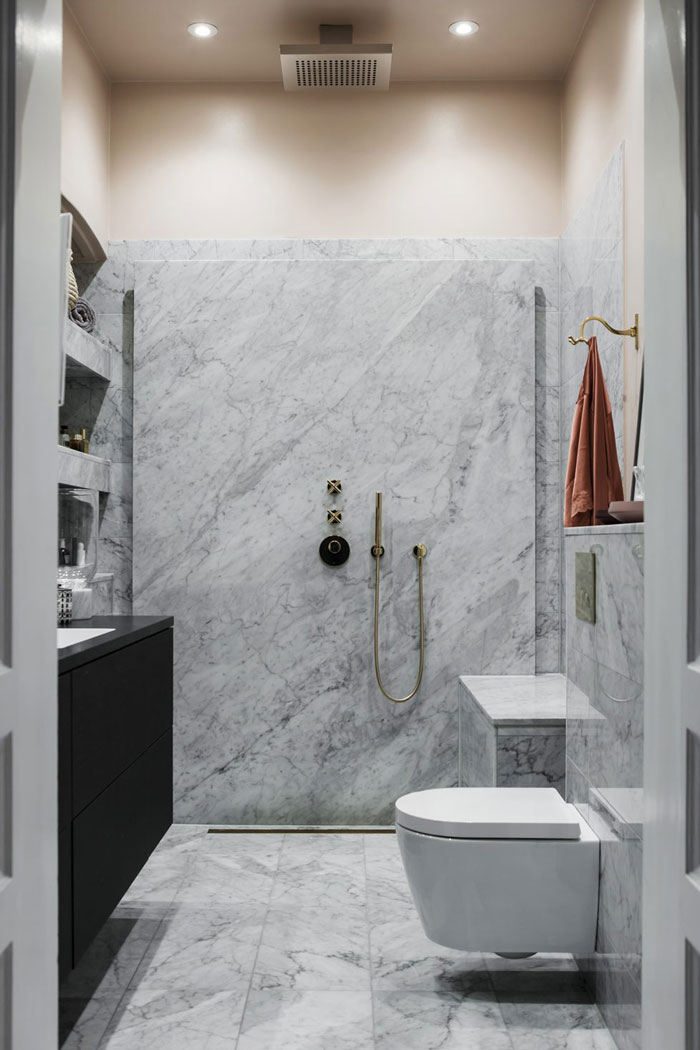 The bathroom is small, clad with white marble and with brass fittings for a chic look