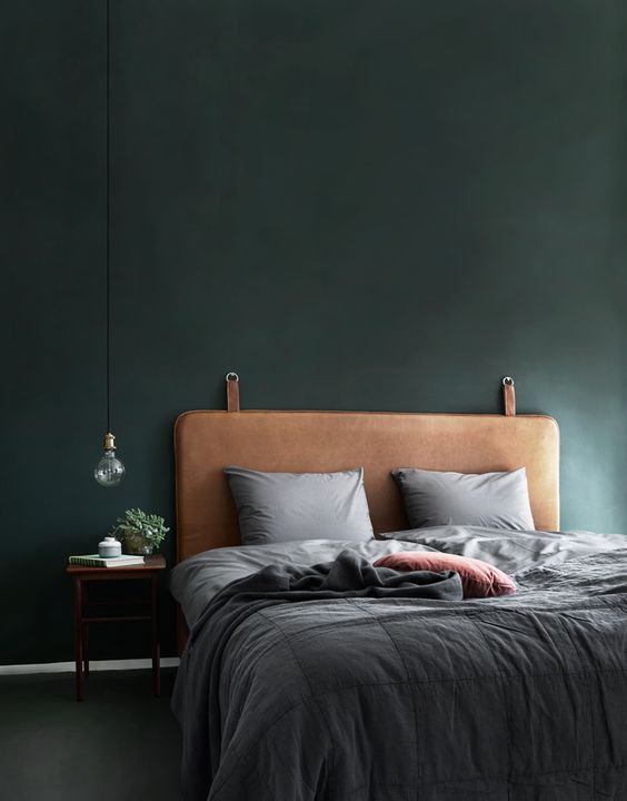 a brown leather upholstered bed with a dark green wall create a manly feel