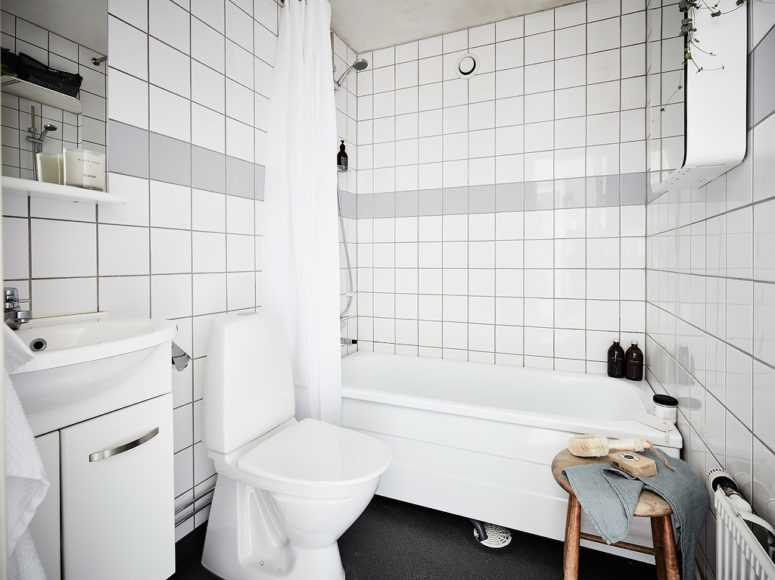 The bathroom is done in white and grey tiles, and a wooden stool adds texture