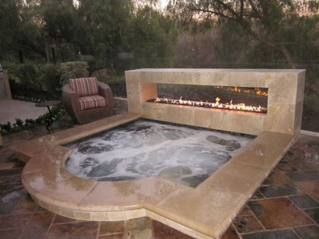 a sunken jacuzzi with a stone edge and a fireplace next to it for a dramatic look