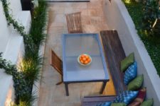16 a small patio with a stained wooden L-shaped bench and a modern glass table