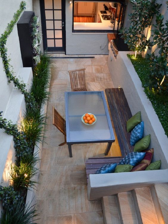 A small patio with a stained wooden L shaped bench and a modern glass table