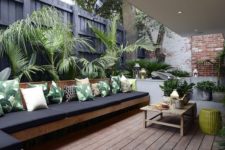 17 a terrace with a long L-shaped bench covered with black cushions and palm print pillows
