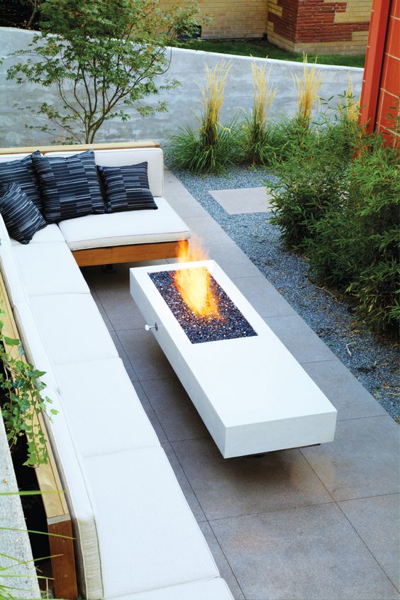 Modern outdoor space with a L shaped bench with white cushions and a modern white table with a fireplace