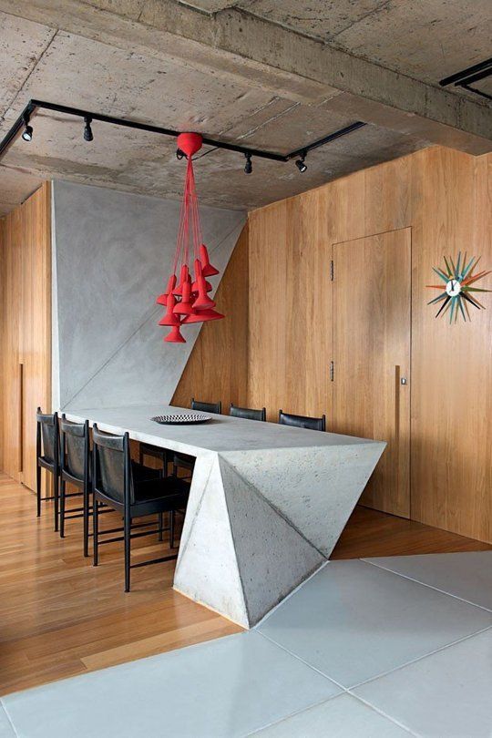 a concrete table with geometric design that goes up the wall and red pendant lamps