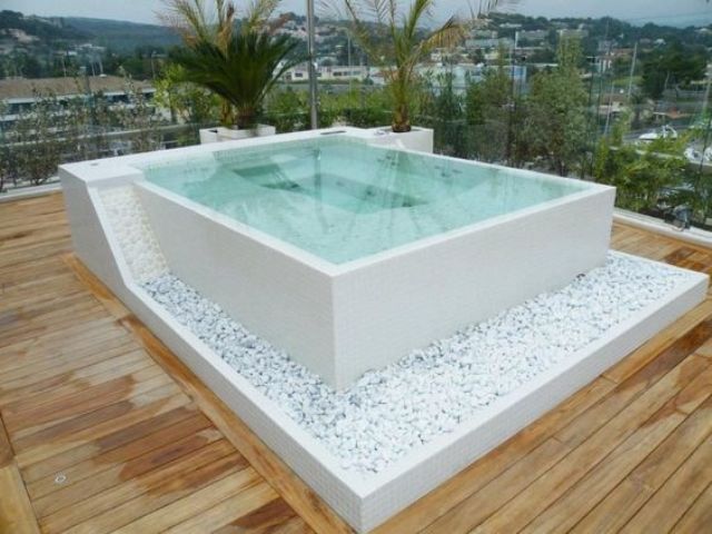 a square jacuzzi decorated with white pebbles on a wooden deck looks very natural and refined