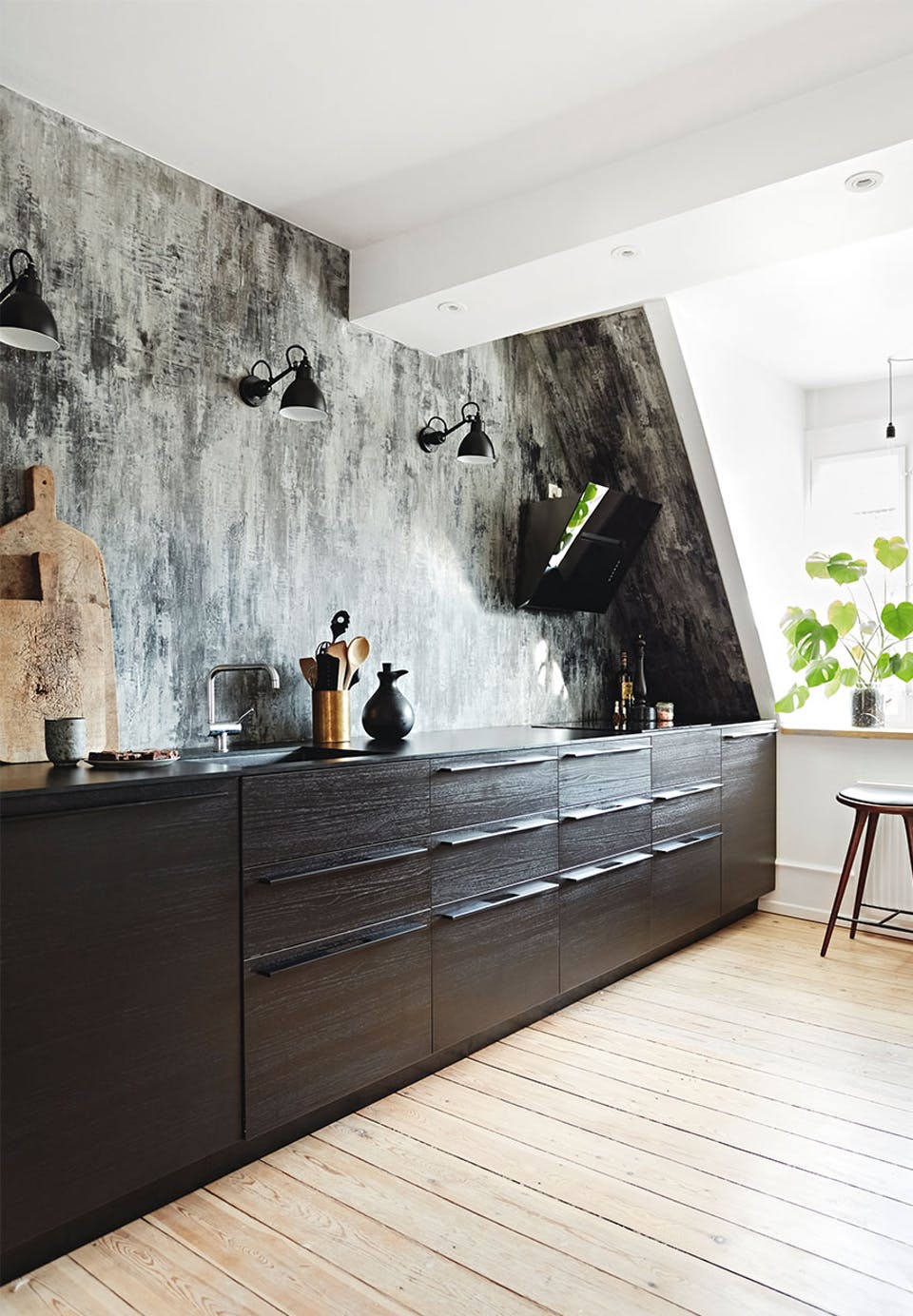 The kitchen features a graphic wallpaper wall as a backsplash, there are black cabinets and wall lamps