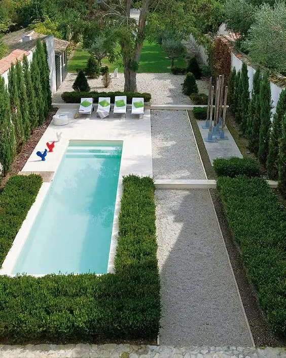 A gravel covered backyard with perfect greenery and a small narrow pool