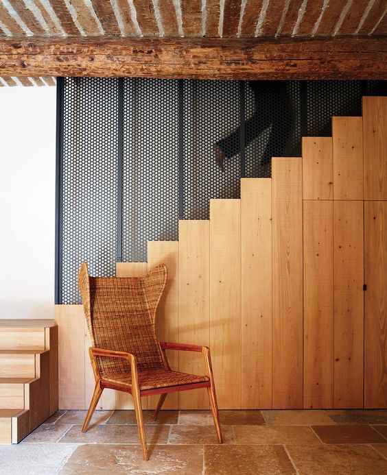 The stairs is made of light colored wood, there's a wicker chair and a restored wooden ceiling for coziness