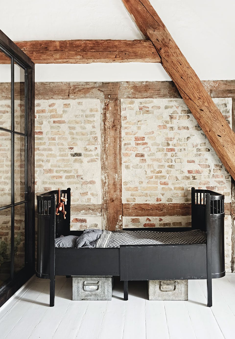 The kid's room is a boy's space, there are beams and brick walls and a vintage metal bed, a metal box under the bed is used for storage