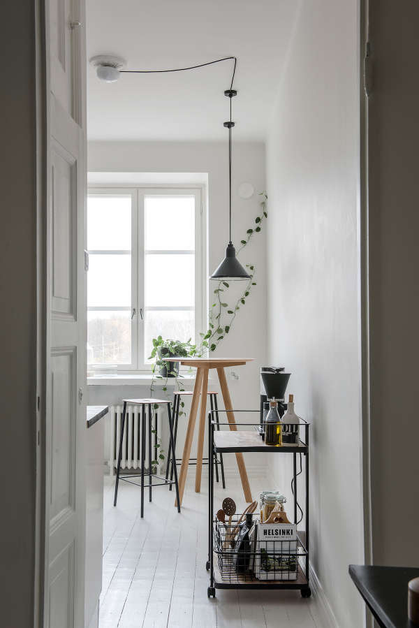 The kitchen is all-white, with tall stools, greenery and a metal bar cart for an industrial feel