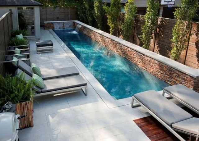 a modern small backyard with a narrow pool with waterfall and a couple of loungers