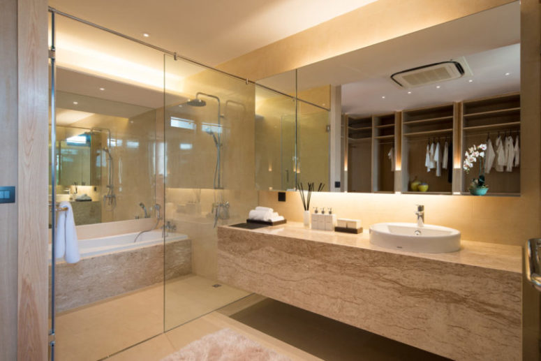 The bathroom is clad with light-colored stone, there's a shower and a bathtub