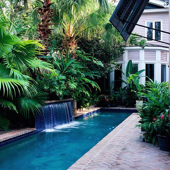brick clad backyard with a lot of greenery for privacy and a narrow pool with waterfalls