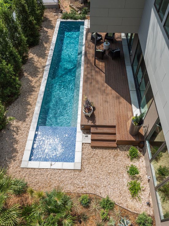 narrow backyard pool clad with white tiles next to a wooden deck