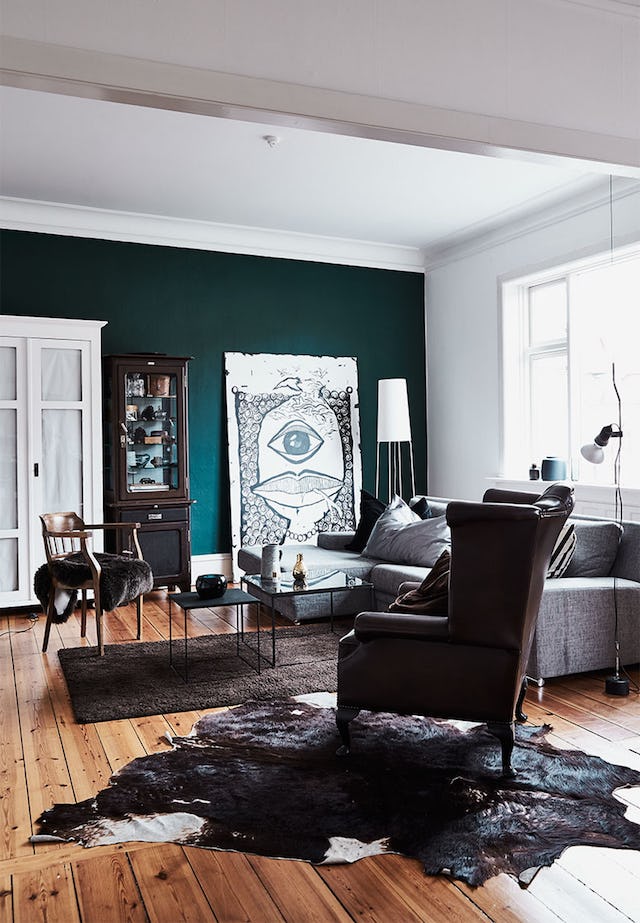 The living room is done in white and teal, with light-colored wooden floors, brown and grey furniture, with a statement wall art piece in black and white