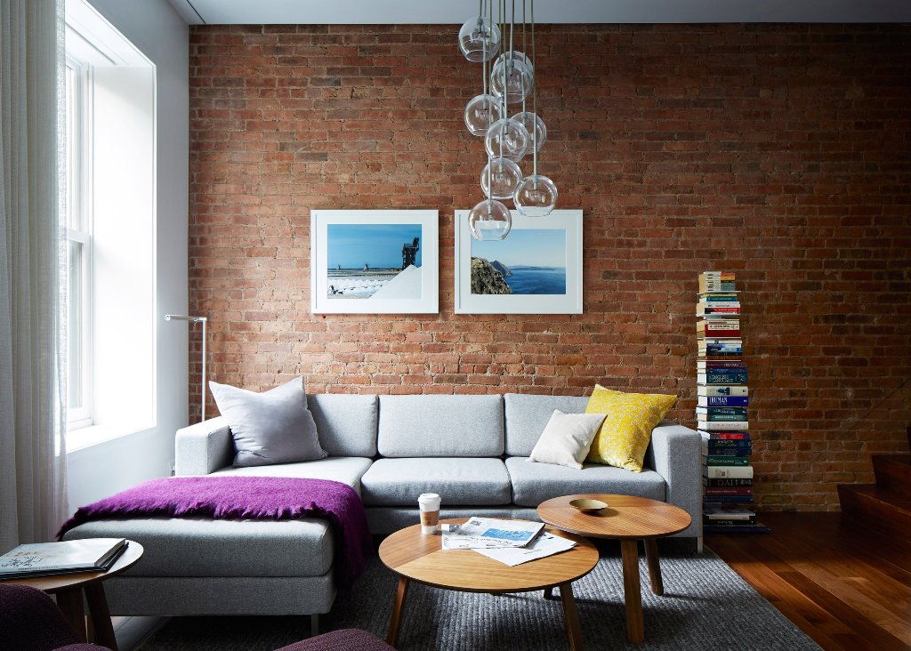 A grey sofa contrasts an exposed brick wall, there's a bubble pendant lamp and an open bookshelf