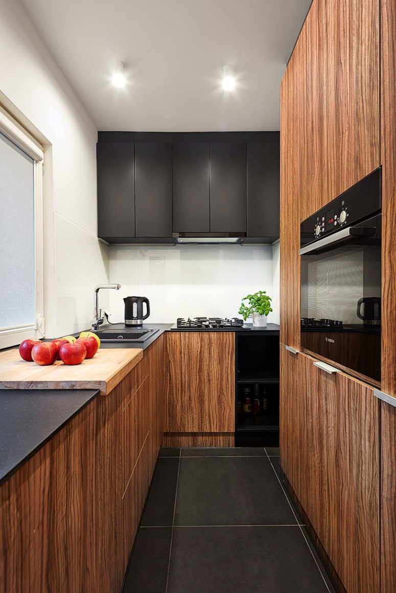 The kitchen is also small, it features white walls and a backsplash and black and warm wood cabinets for a contrasting look