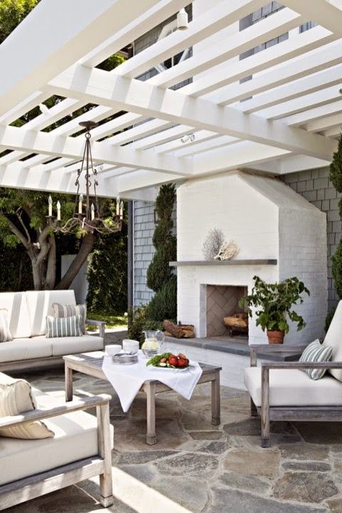 A coastal inspired outdoor living room with a chandelier and a fireplace and neutral upholstery