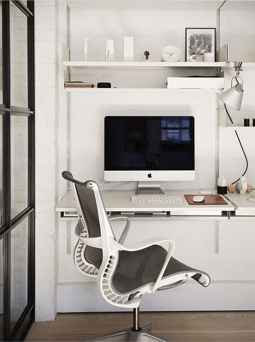 A small home office nook is done in pure white, with a chic modern chair and some shelves