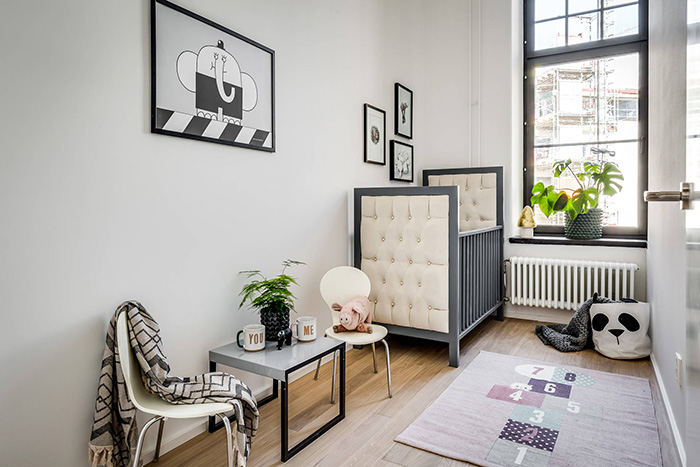 The nursery is creamy and grey, with an upholstered kids bed, a cozy rug and some artworks