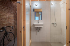 08 The bathroom is neutral, with white tiles and a concrete floor, wood makes it cozier