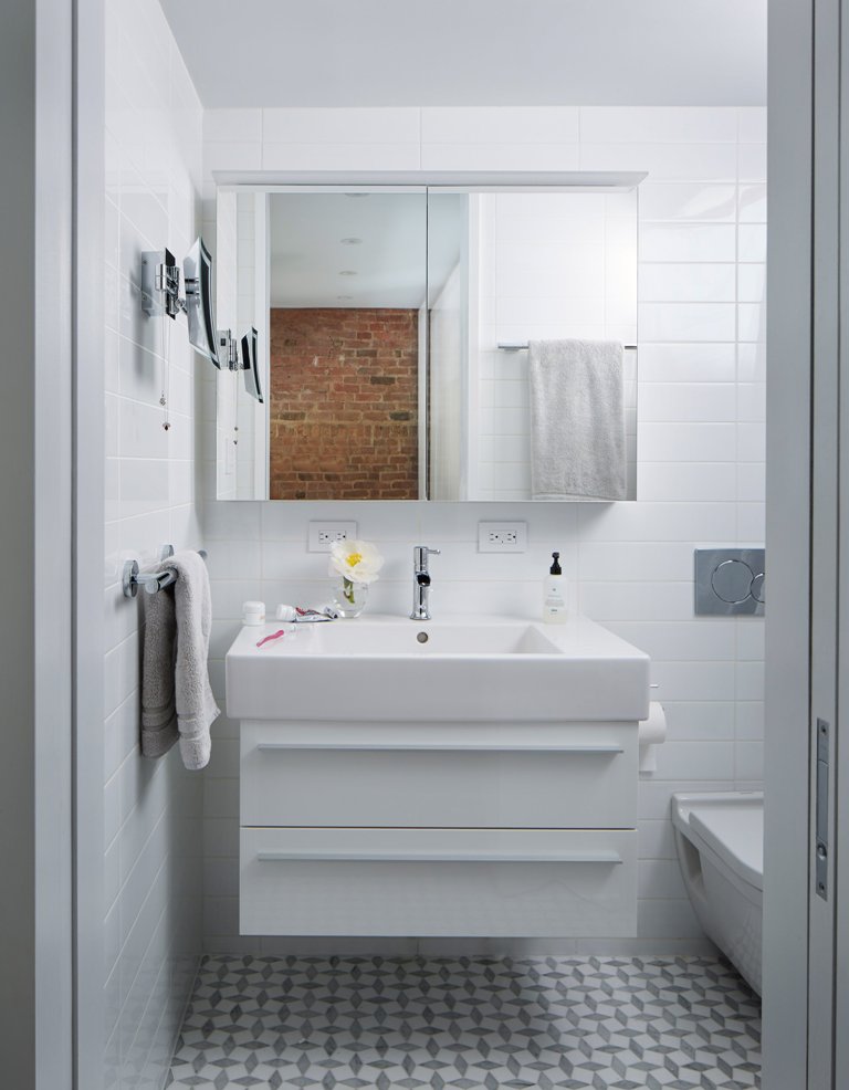 The bathroom is clad with white tiles, and the floor is done in grey graphic tiles, everything here is functional