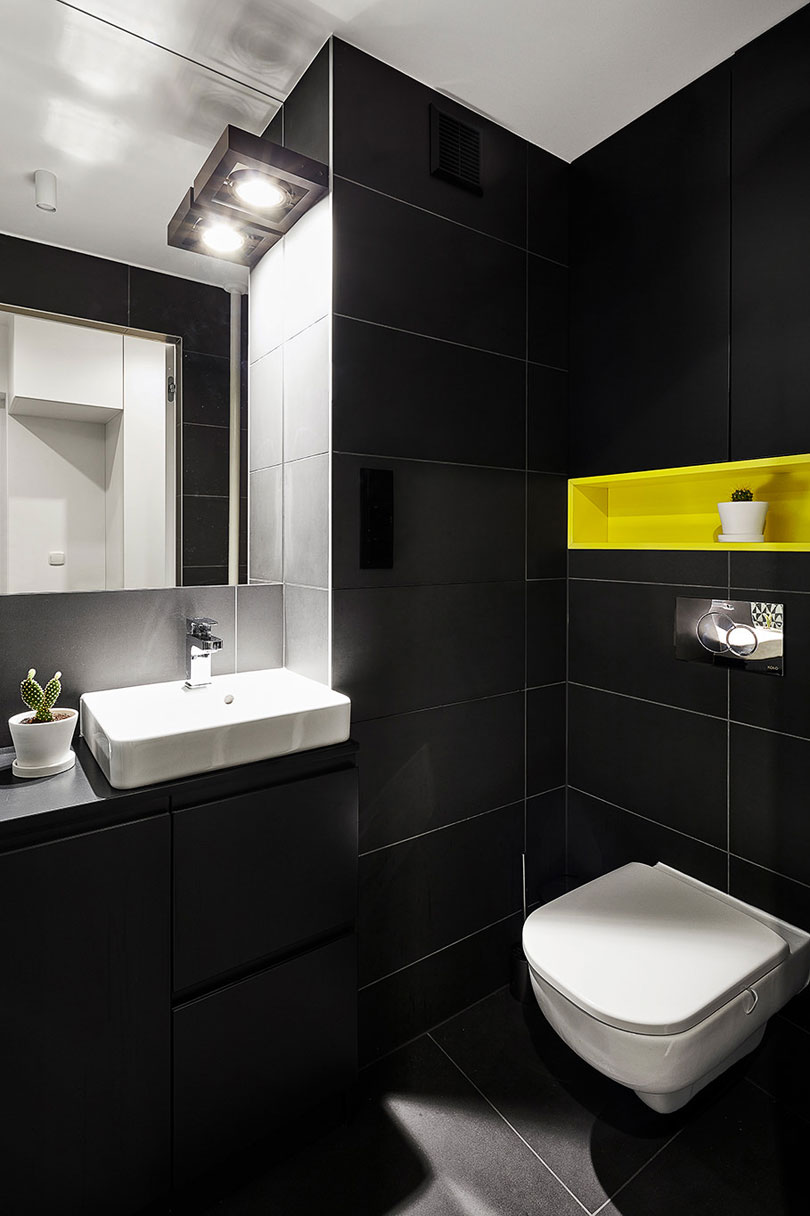 The matte black monochromy is broken with a neon yellow built in shelf over the toilet