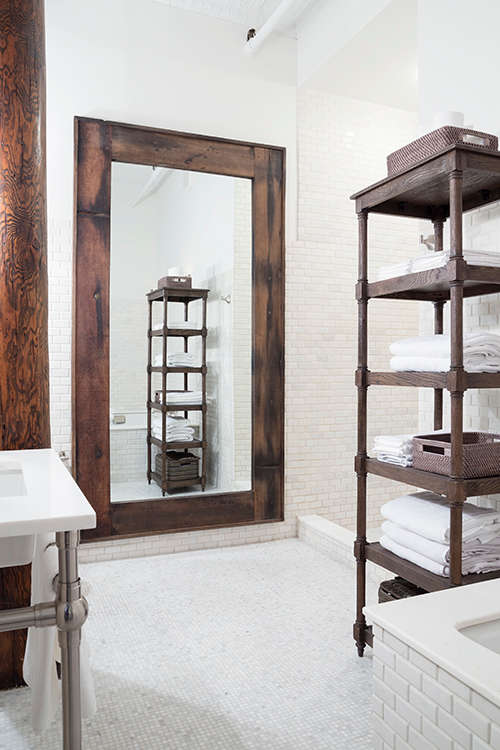 The bathroom is clad with white tiles, and the accents are made with dark stained wood and dark metal