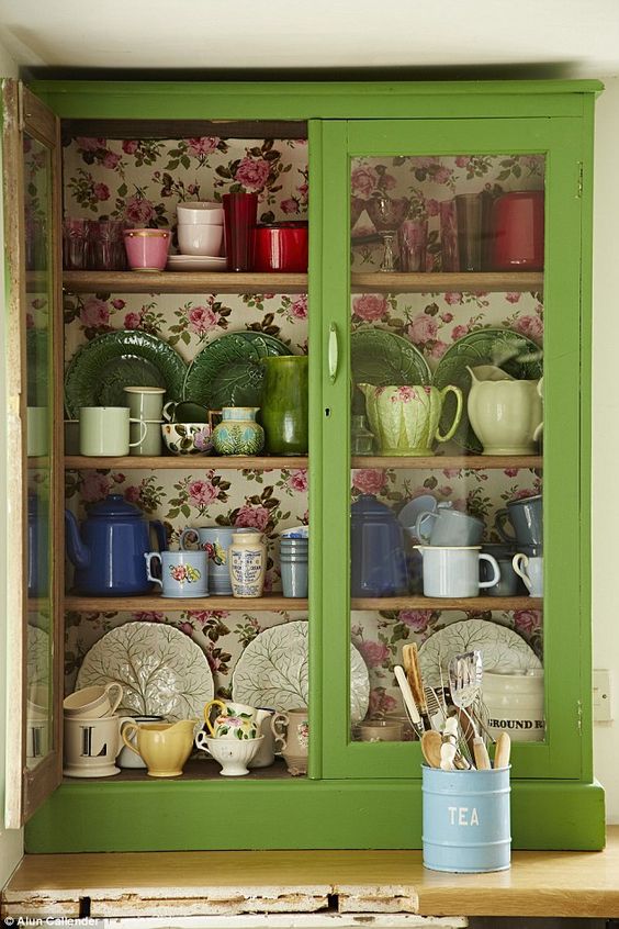 a green glass cabinet with colorful floral wallpaper inside for a chic look